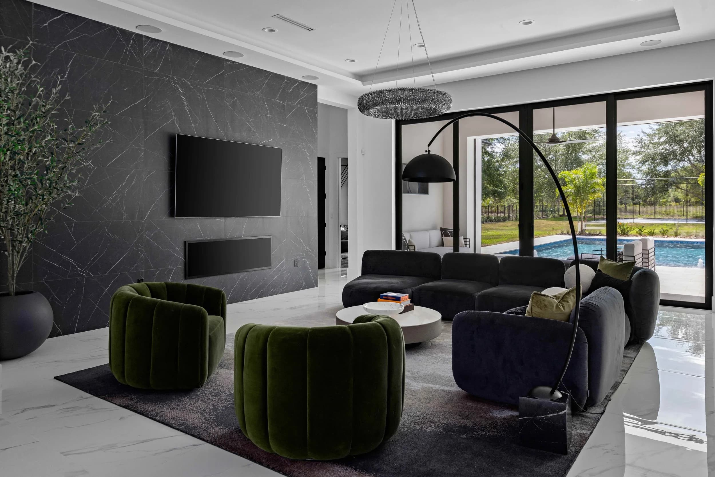 Great room of a modern Orlando estate with a honed stone feature wall, velvet seating, and glass doors opening to the pool